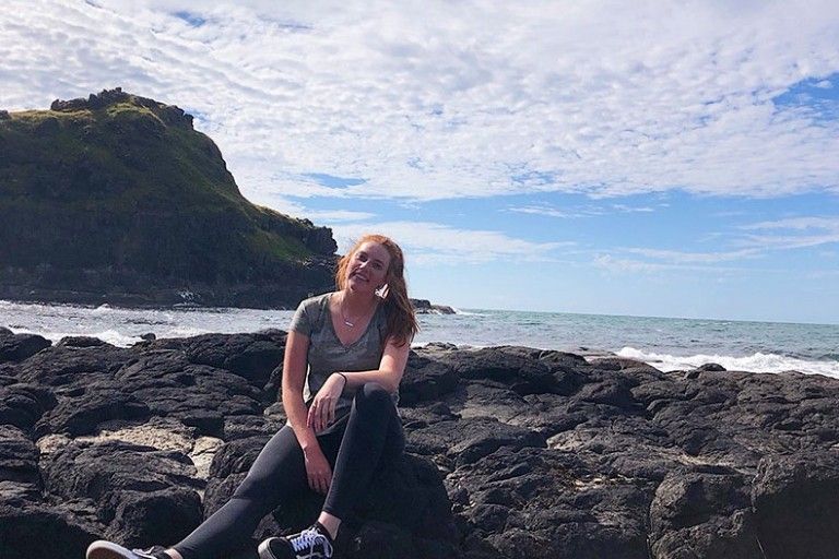 Katie Rodwell sitting on a rocky beach on the coast of Ireland with the ocean in the background.