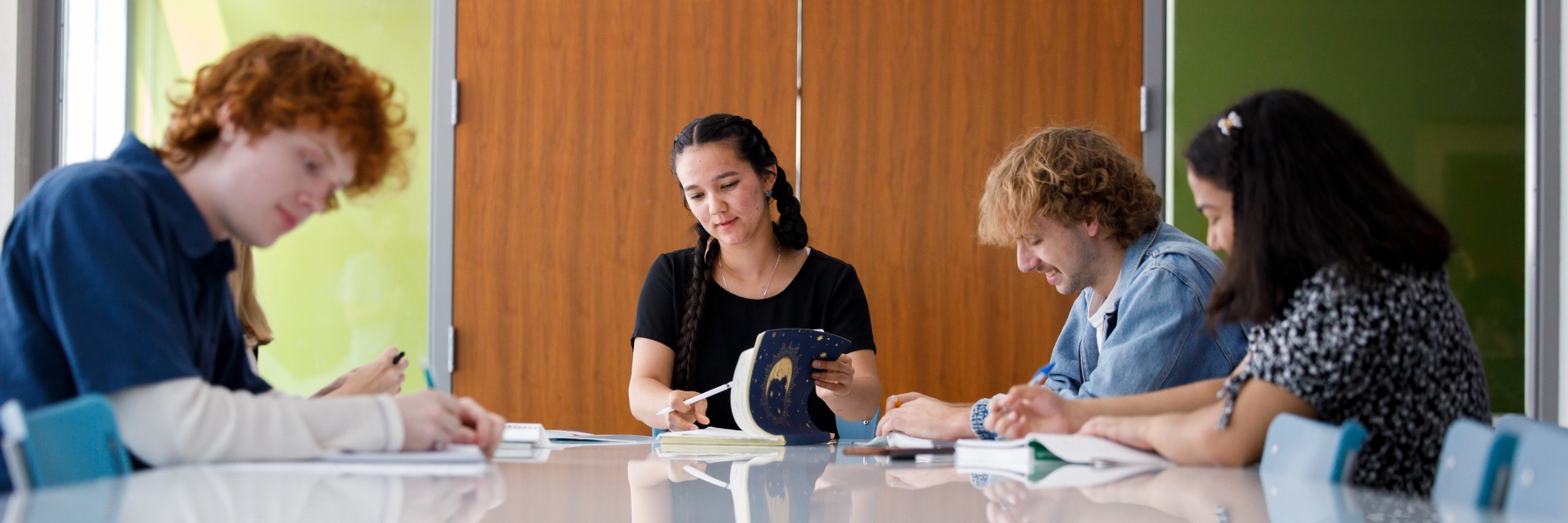 Students sit around a table and take notes while conversing with each other
