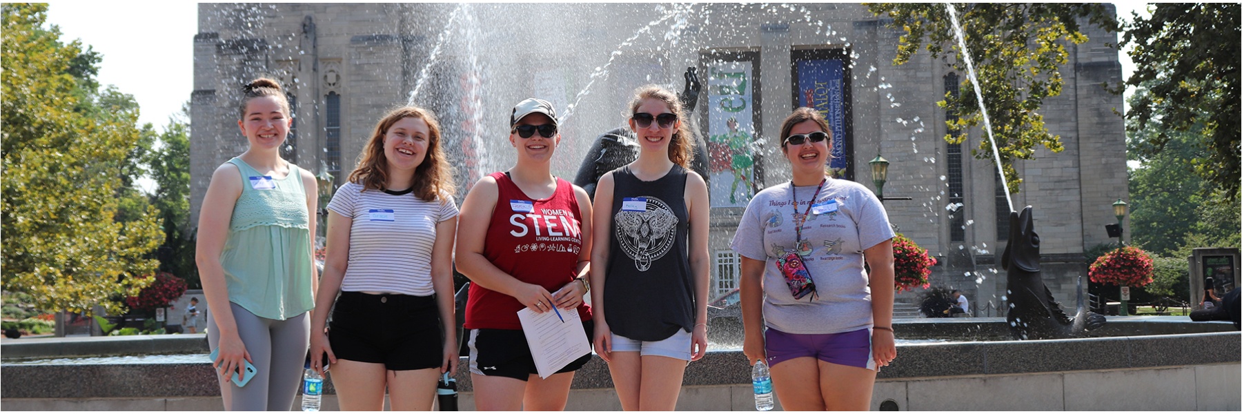 Women students standing in front of a fountain and smiling