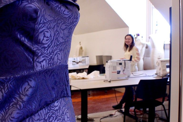 Close up of a purple dress with fashion design student Beth Maben looking at it in the background