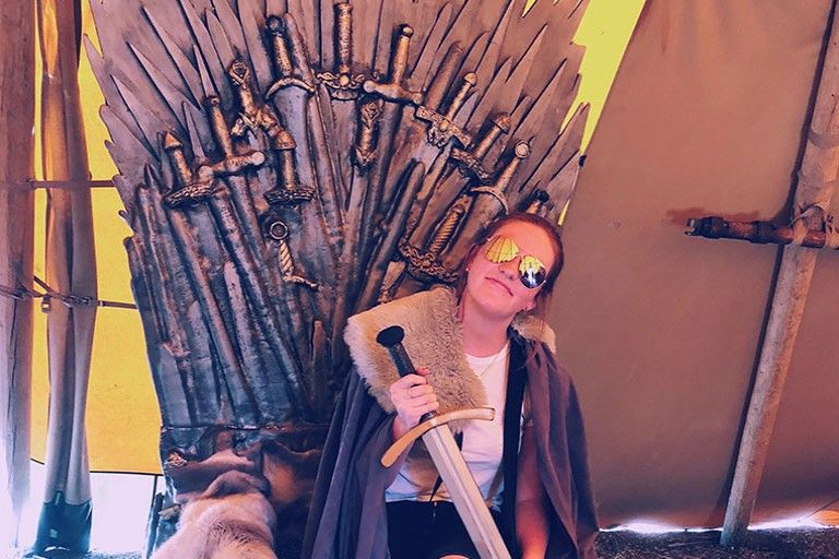 Katie Rodwell sitting on the Game of Thrones Iron Throne, holding a sword